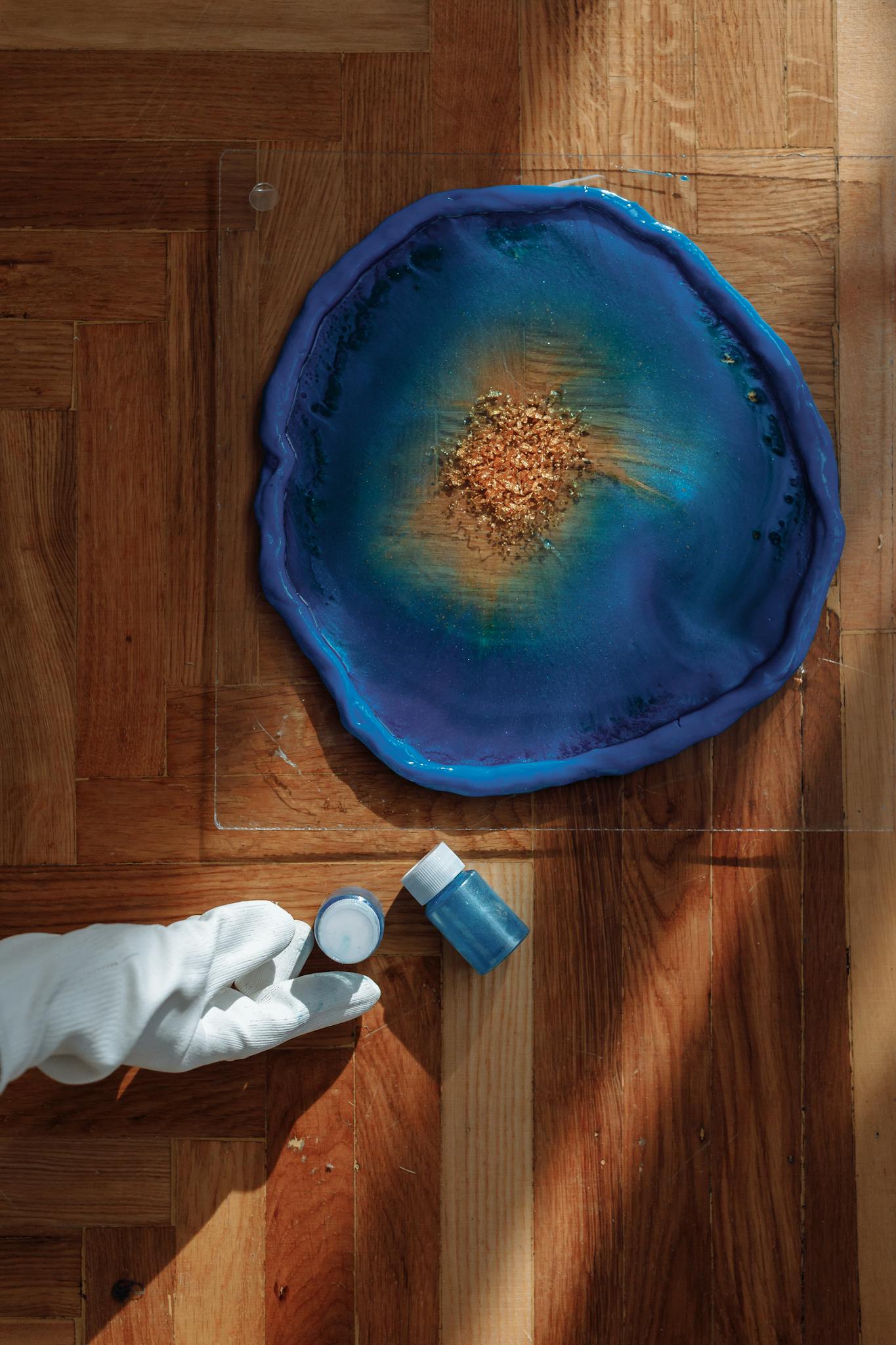 Photo by Thirdman Colorful resin artwork displayed with artist holding pigment jar on wooden floor.