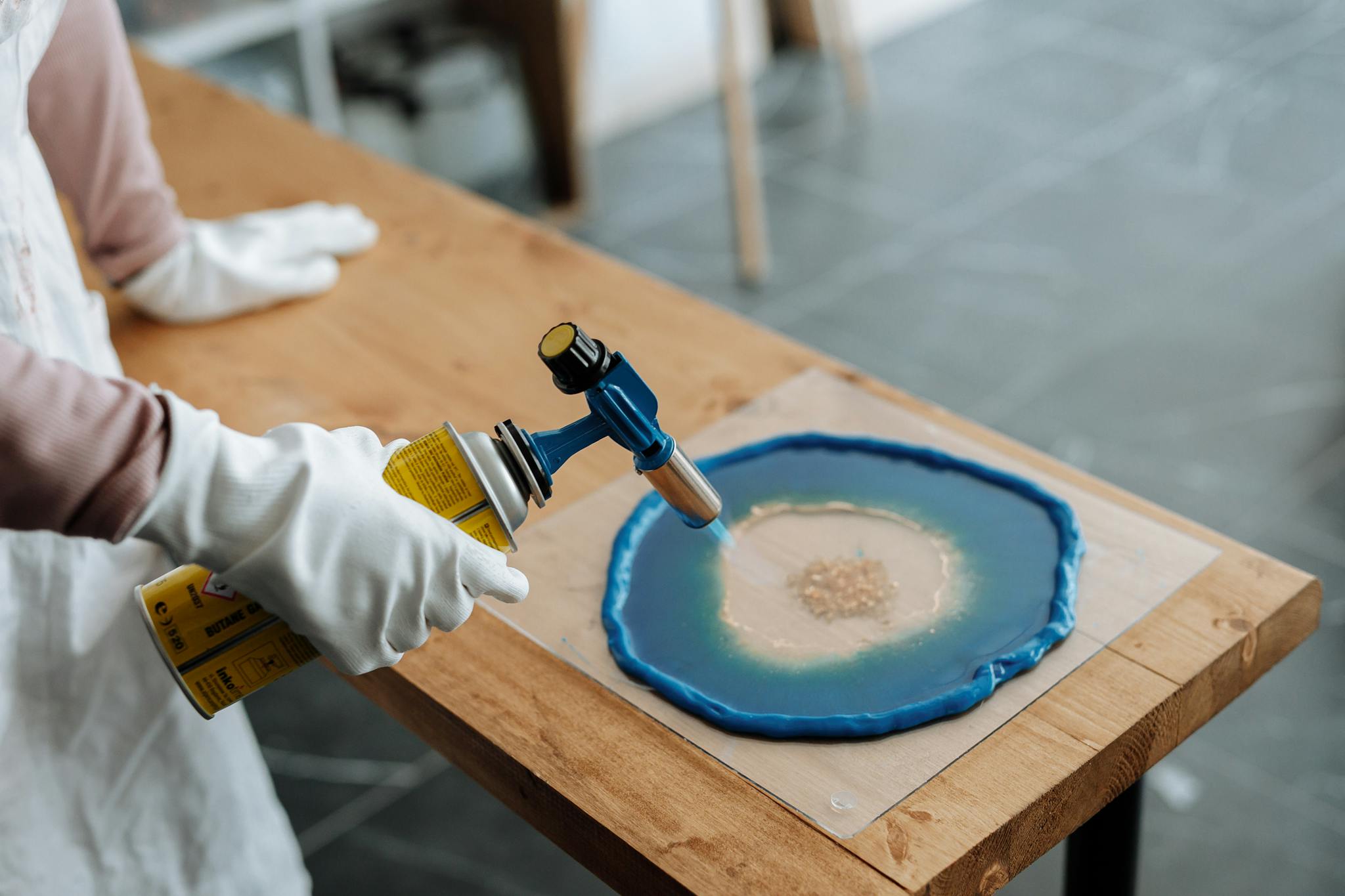 Close-up of hands using blowtorch in resin art on wooden table.