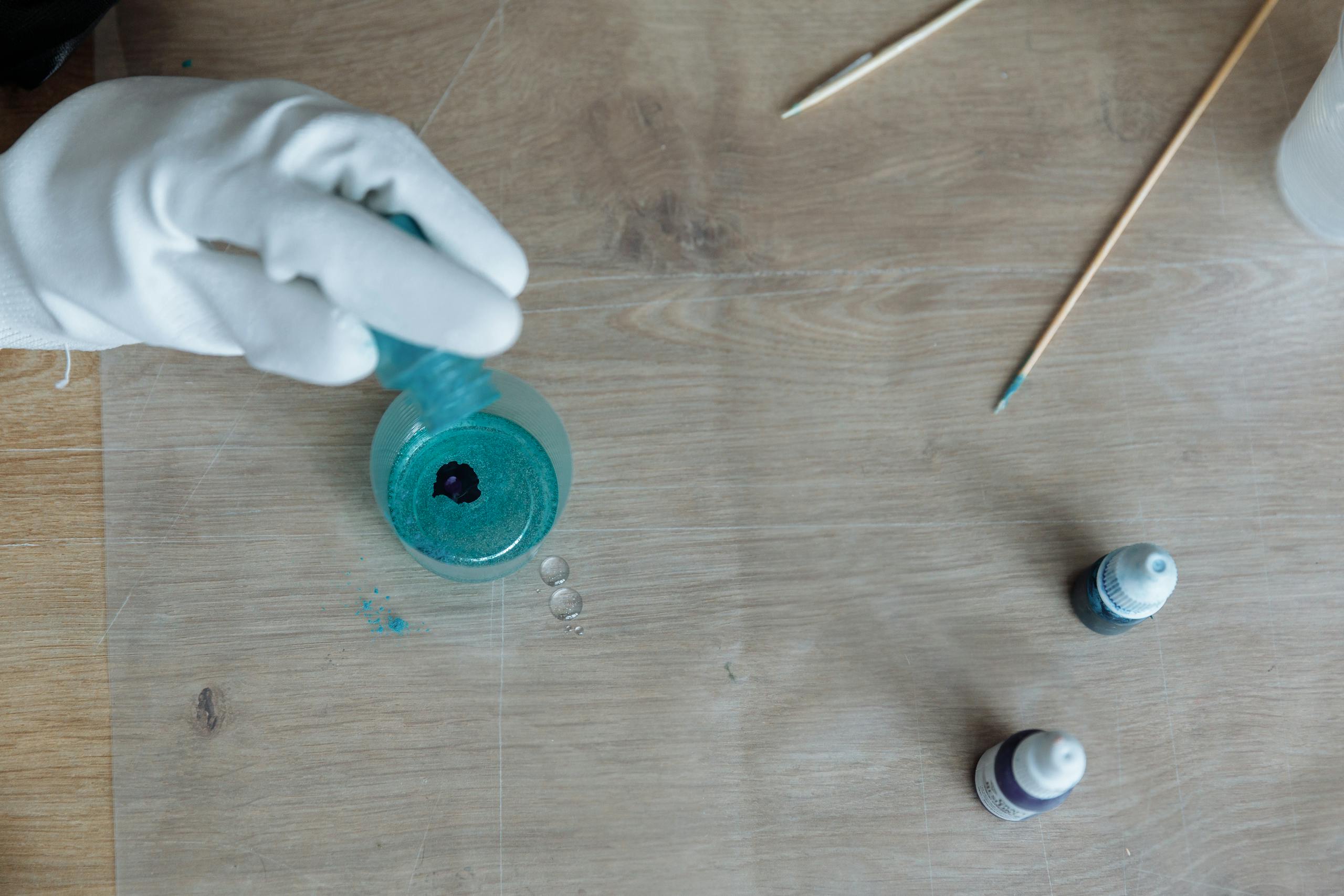 Main gantee versant de la resine bleue dans un moule sur une table en bois