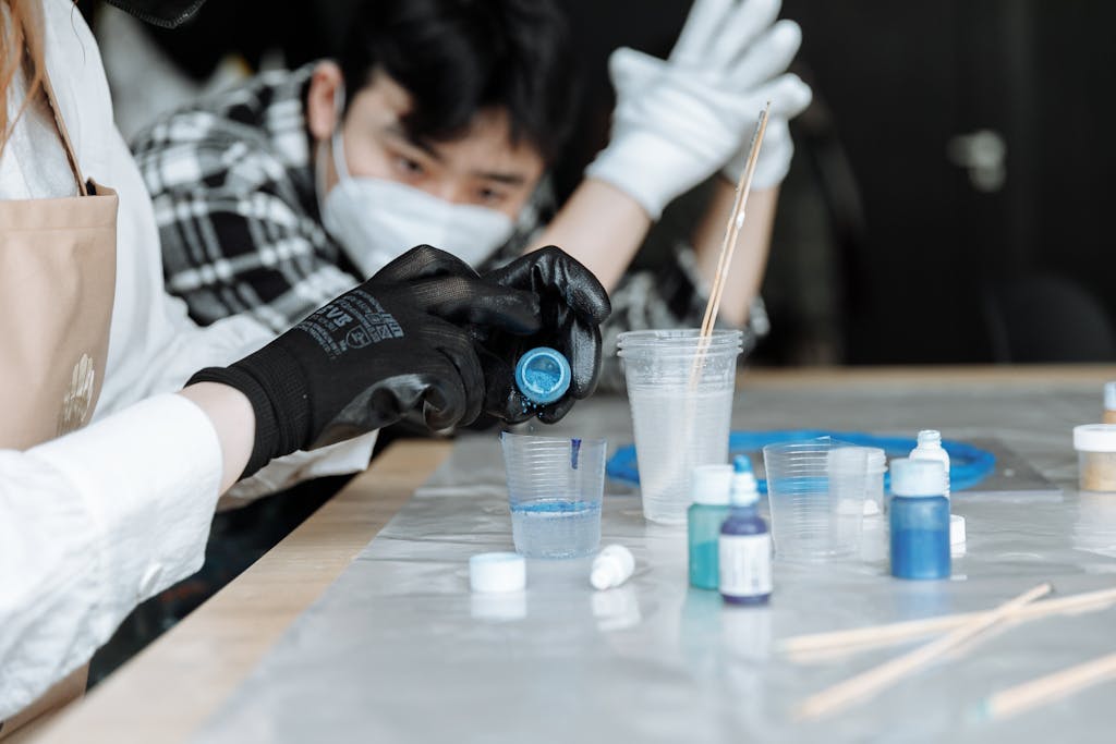 Two people collaborating in an indoor workshop, mixing vibrant colored liquids for an artistic project.